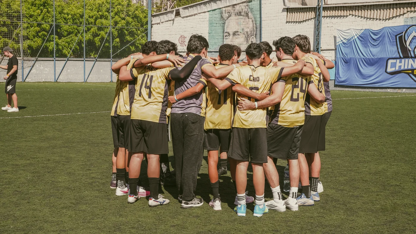 Jogadores de uma equipe com uniformes amarelos reunidos em roda, de braços sobre os ombros