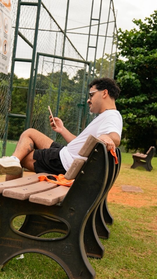 Pessoa consulta o celular sentada em um banco ao lado da quadra